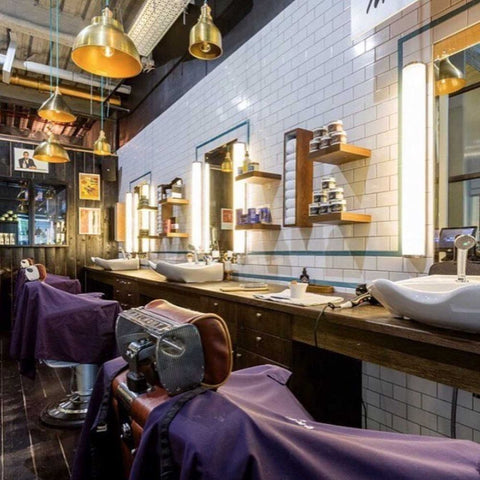 A salon with tiled walls and vanity mirrors and brass industrial pendant lights