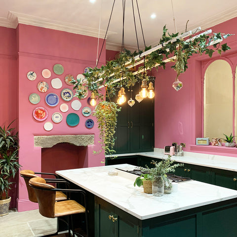 A pink kitchen with decorative plates on the wall and hanging plants