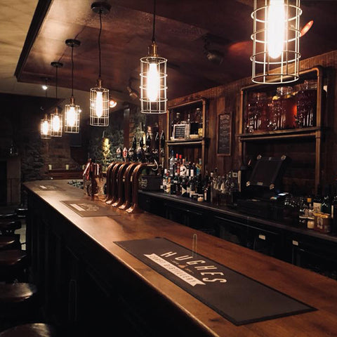 A dark bar with wooden surfaces and hanging cage lighting