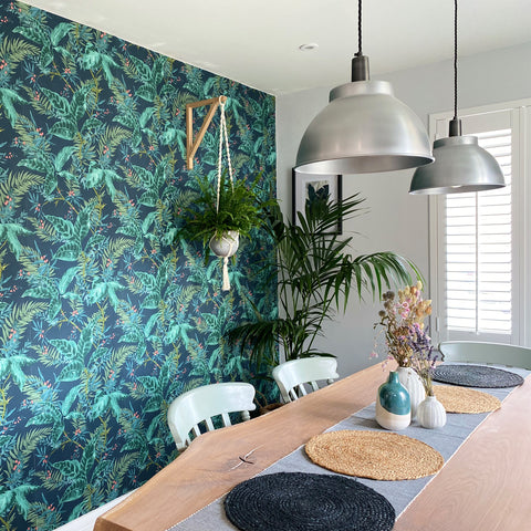 A dining room with leaf-patterned wallpaper, woven placemats and macramé baskets