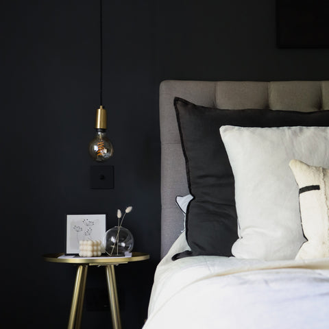 A bedroom with black walls, white bedding and a hanging light