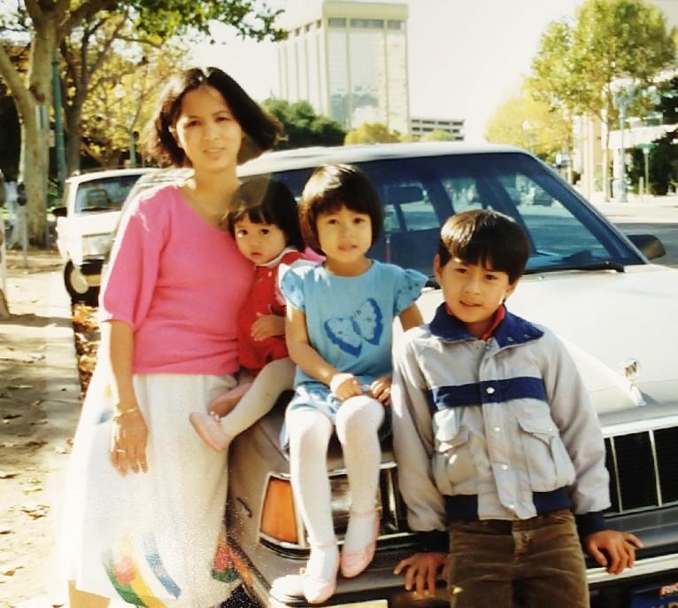 Archival photo of Susan Lieu, her mother, and her siblings sitting in front of a car.