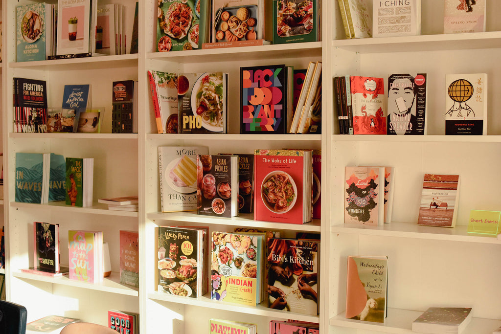 White bookshelves lined with books by Asian American authors at Mam's Bookstore. This photo in particular highlights the cooking section.