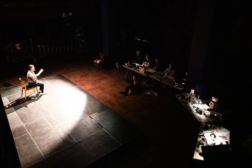 Susan Lieu sitting on a chair on stage with the spotlight on her as she performs her one woman show "140 Lbs: How Beauty Killed My Mother."