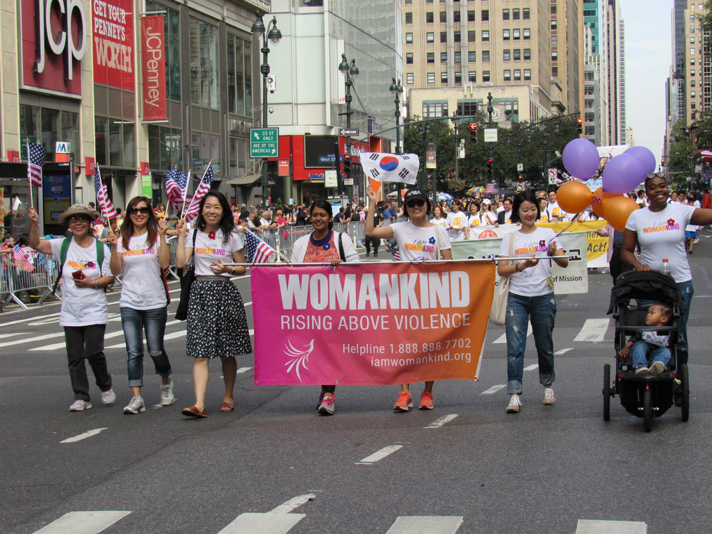 Women peacefully protesting in the street holding up a Womankind banner in support of survivors of gender-based violence.