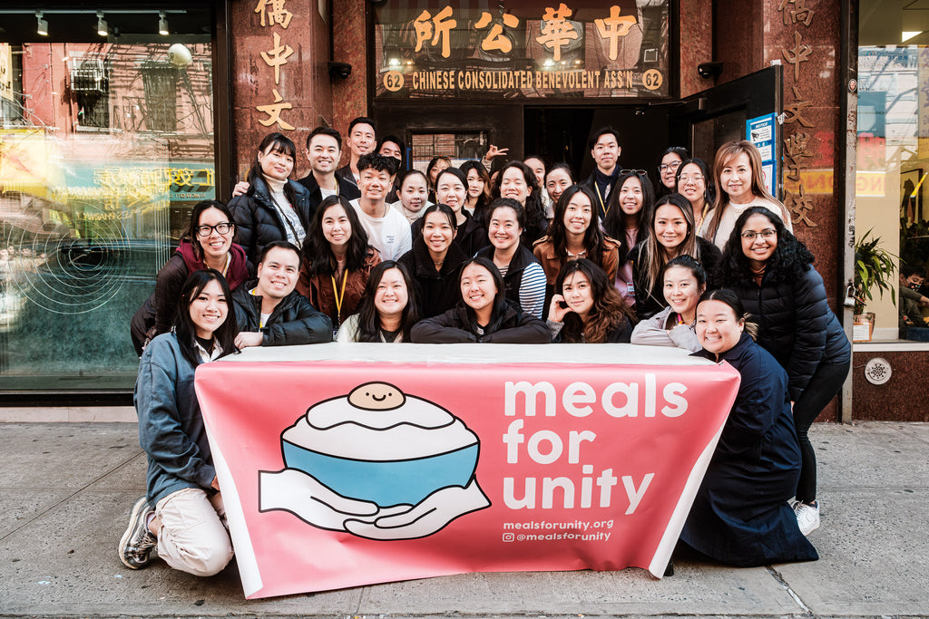 A group photo of the Meals for Unity team with a large branded banner.