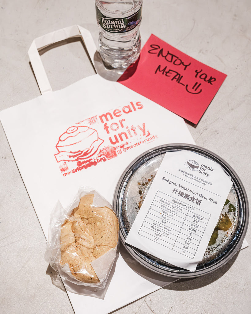 Closeup image of they type of meal that is distributed at a Meals for Unity event. The meal is packaged in a plastic container with an Asian dessert and bagged in a white branded bag.