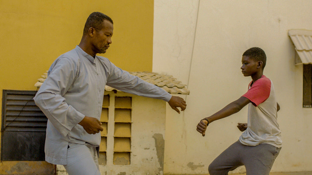 A man and a child sparring with one another against a yellow building.