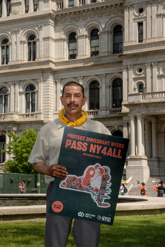 A man holds a sign reading "Protect Immigrant NYers. Pass NY4ALL."