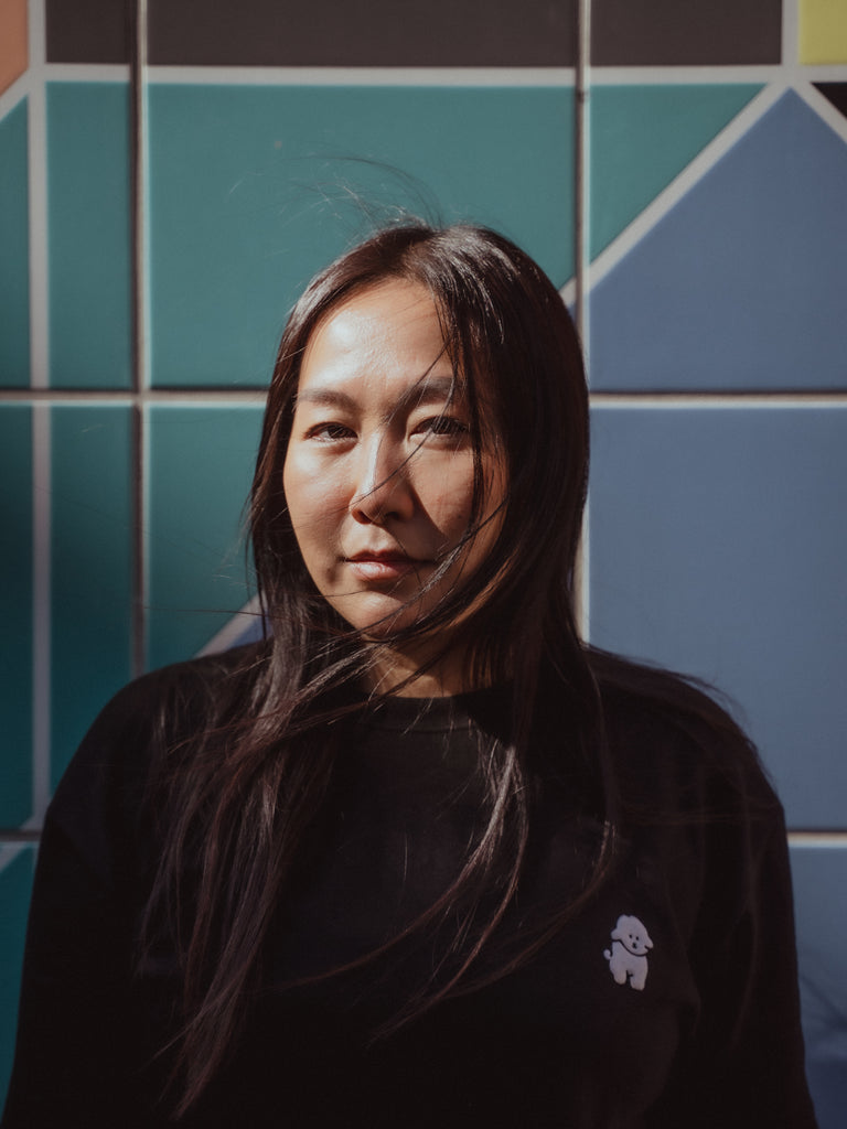 Graphic designer and creative director Thi Huong Truong standing against a colorful tiled wall standing partly in the shadow. 