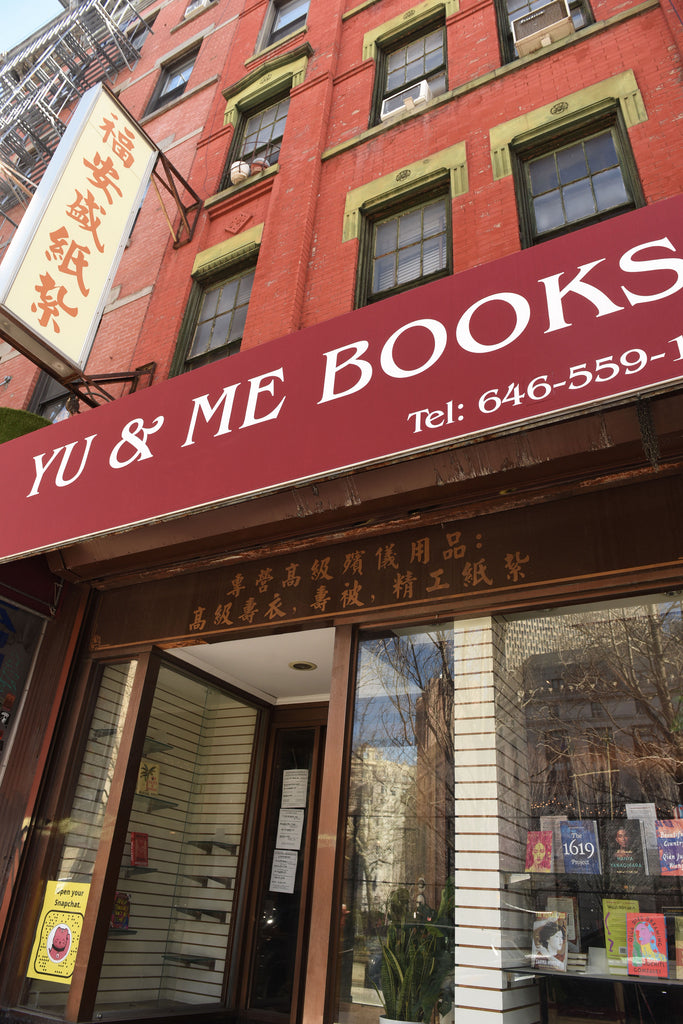 Yu & Me Books storefront with a dark red awning with he bookstore name on it. The windows and door are made of glass and books are displayed in the window. 