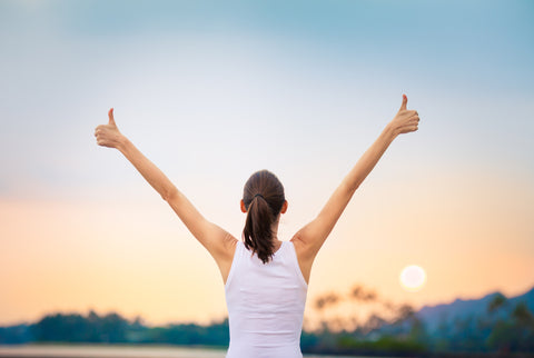 A woman with her hands in the air and back to the camera at sunrise. 