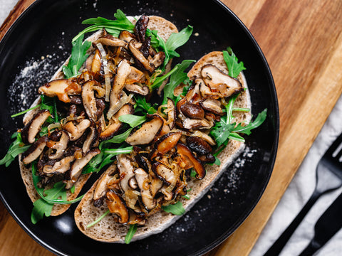 Bird's eye view of mushroom on toast. The toast is on a black plate atop a wooden table.