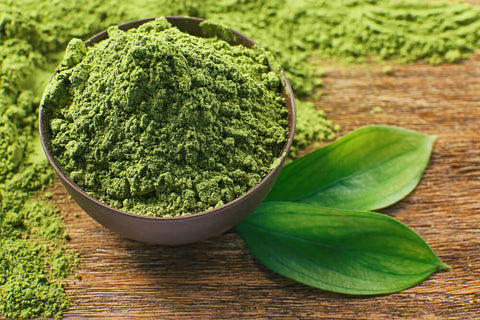 A bowl of powdered matcha on a wooden table, with two tea leaves