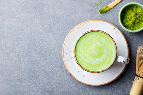 A bird's eye view, looking down at a warm cup of matcha tea. The bench is concrete/grey.