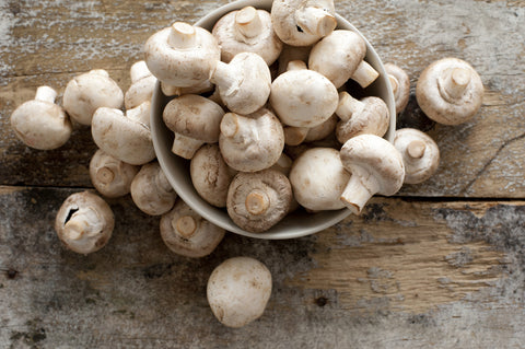 A bird's eye view of a bowl of button mushrooms on a wooden table