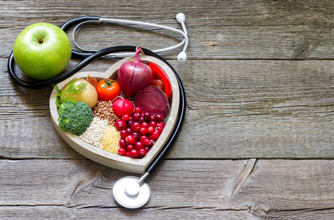 A heart-shaped bowl on a wooden table. The food in the bowl is a mix of grains, fruit and vegetables. 