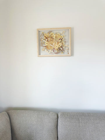 Amelia's 16x20 gray wood pressed flower frame hung up in her living room.