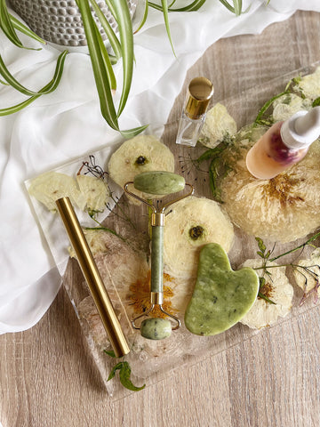 Jade roller, perfume bottle, and skin tonic displayed on a pressed floral resin tray.