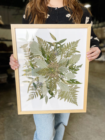 Woman holding a pressed and framed all greenery bouquet.