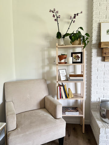 A cozy reading nook featuring an armchair and a bookshelf. A mini pressed flower frame sits on the bookshelf.