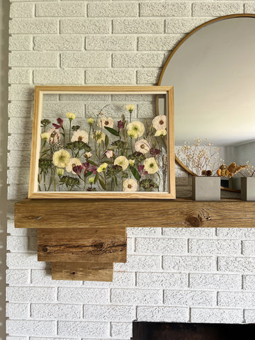 Pressed and framed artwork featuring roses, alstroemeria, and lisianthus displayed on a mantle alongside a round mirror.