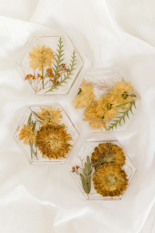 Pressed flowers in resin coasters against white linen.
