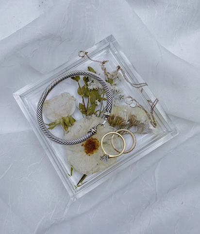 Pressed flowers in a resin ring dish with jewelry on top against white linen.