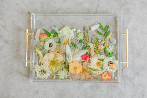 Pressed flowers designed in a field like design inside a resin serving tray against concrete.