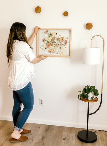 Woman hanging her pressed and framed wedding bouquet in her home.