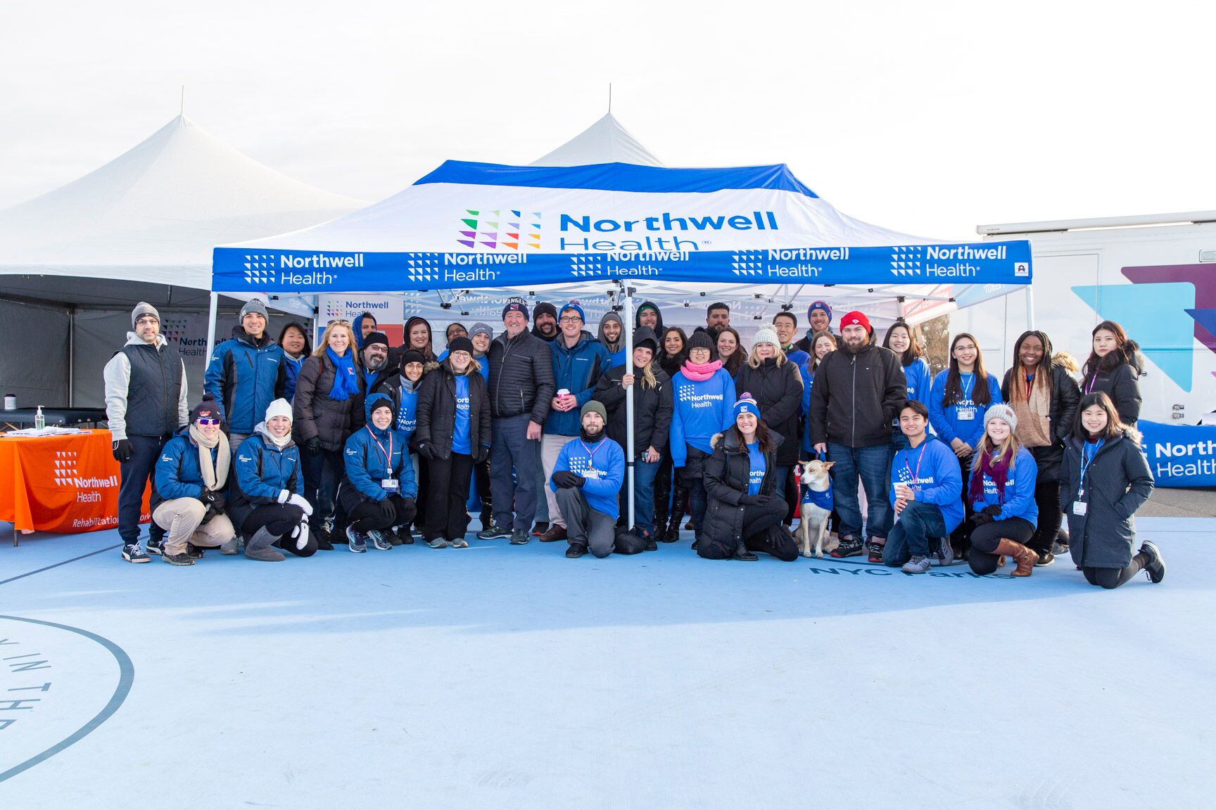 a group of cheerful individuals posing in front of a spacious 10x20 canopy tent emblazoned with the 'Northwell Health' logo