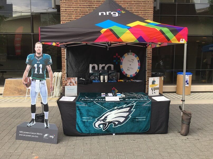 nrg outdoor booth set up with cutout cardboard of an nft player, custom canopy and table with fitted cover