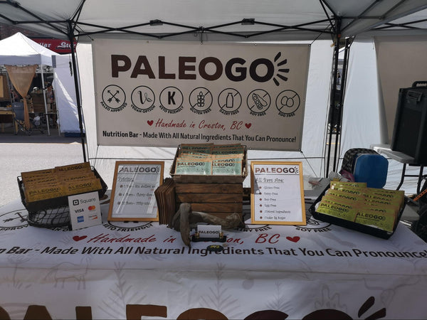 PALEOGO stall showcasing nutrition bars that are handmade in Creston, BC, with clear indications of being paleo-approved, dairy-free, keto-friendly, gluten-free, soy-free, and egg-free