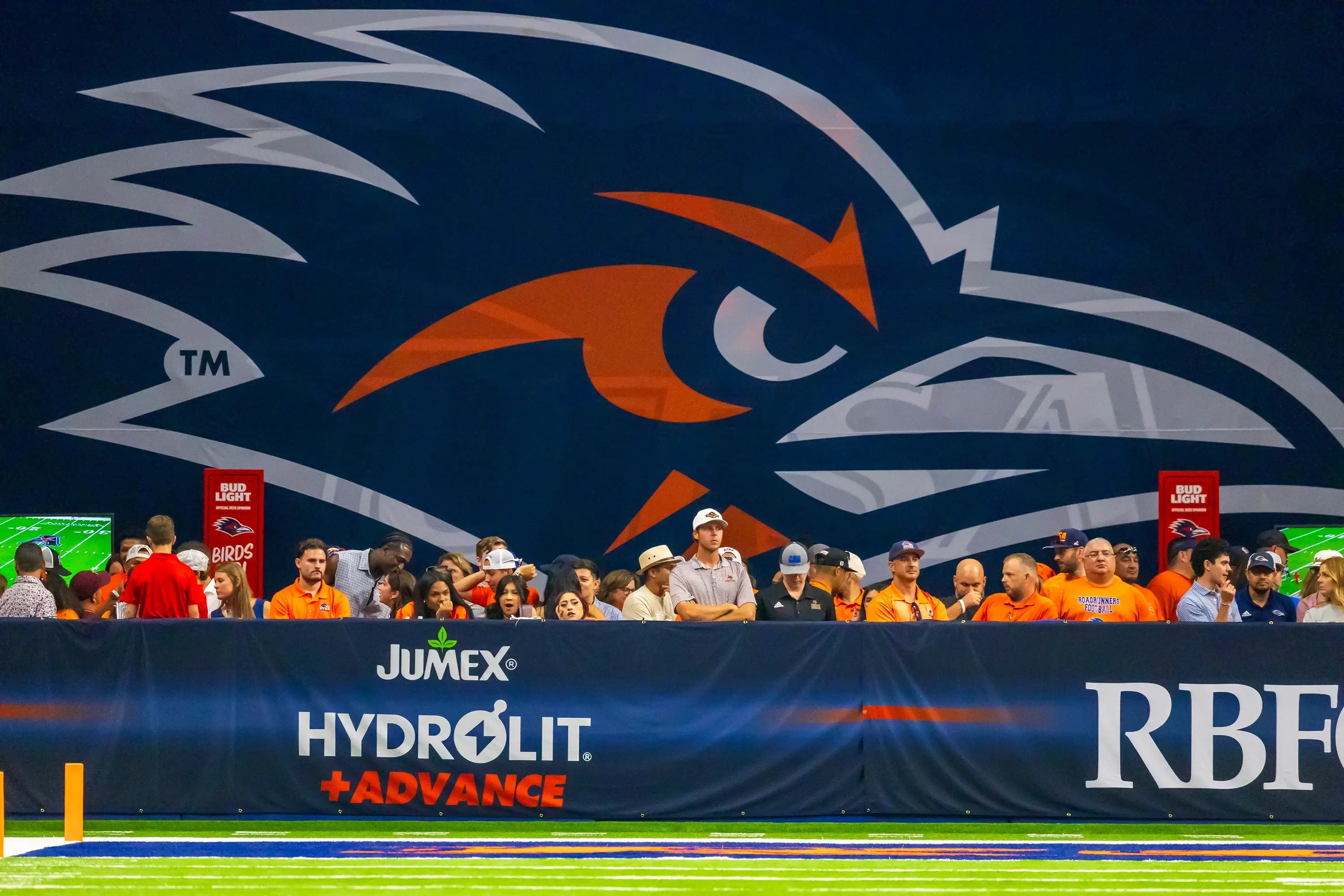 UTSA Roadrunners sideline at the Alamodome with large Roadrunners logo and field-level wall branding for Jumex and Hydrolit Advance
