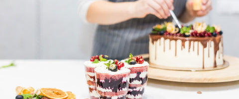 pastry chef applying final touches on a cake with desserts in the foreground