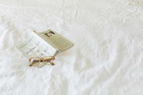 White Linen Sheets on top of a bed, with glasses and a book on top