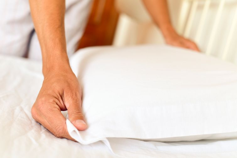 Older man placing bamboo pillowcase on clean, white sheets