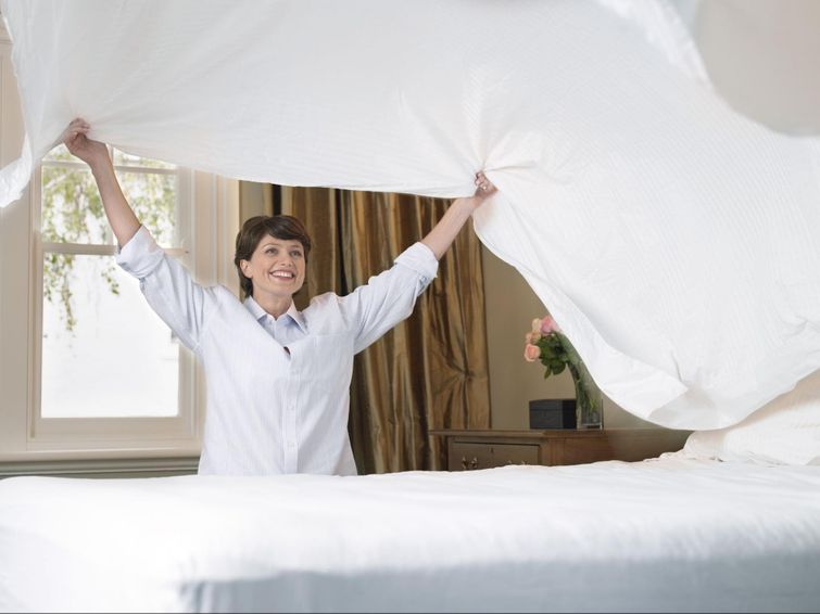 Smiling woman spreading freshly-cleaned bamboo bed sheets on bed