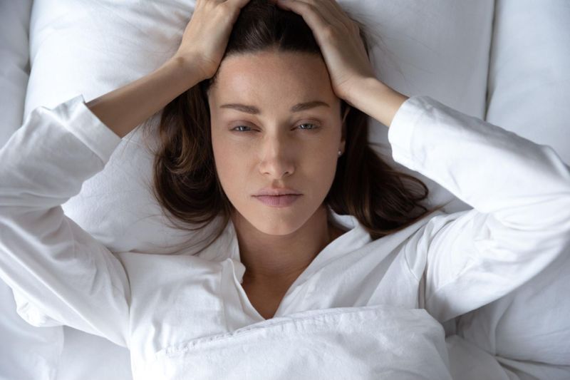 Exasperated woman with insomnia grasping forehead with hands