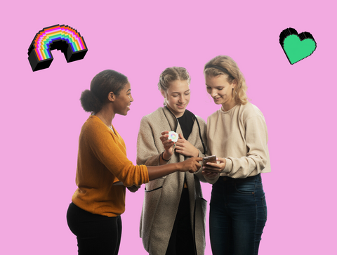 Three girls look at a small device called an imagi Charm. There is a pink background.
