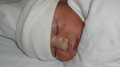 newborn baby dressed in white hat and blanket