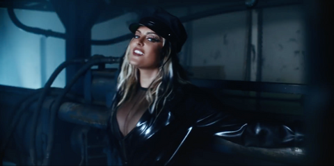 Artist Bebe Rexha walking through a wearing house wearing a black Vex trench and hat for her music video