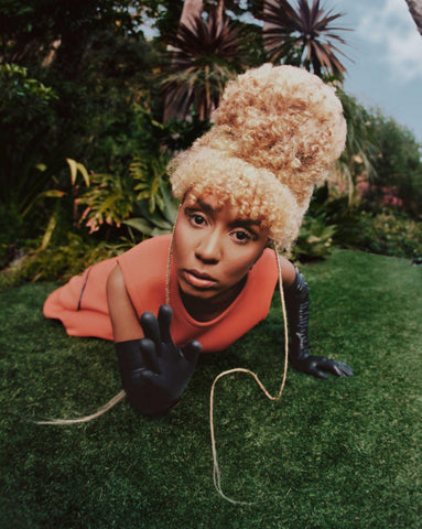 Woman laying in the grass with an orange dress and Vex black latex opera gloves posing for a photoshoot