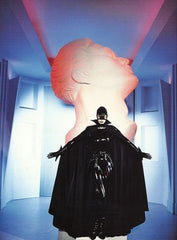 Theirry Muglas black latex caped woman in front of statue. 
