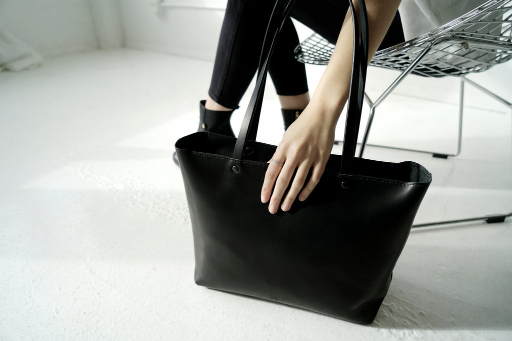 Large black leather tote sits next to female model