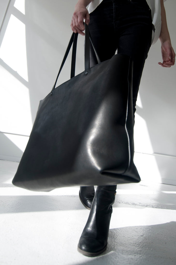Female model walks with large black leather tote in hand