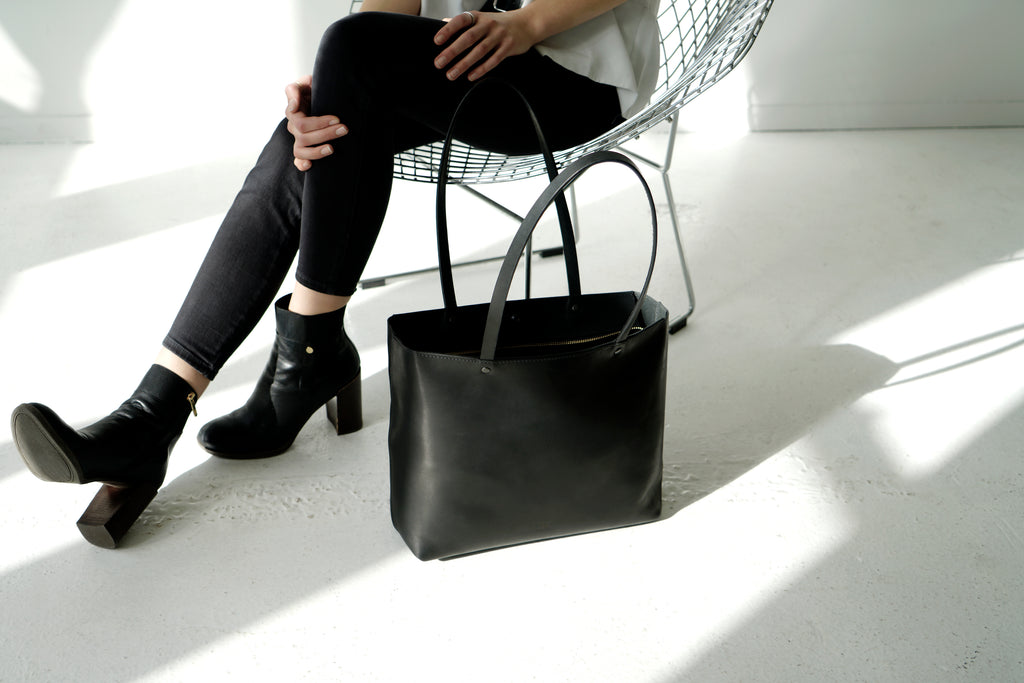 Female model sits with large black leather tote next to her.