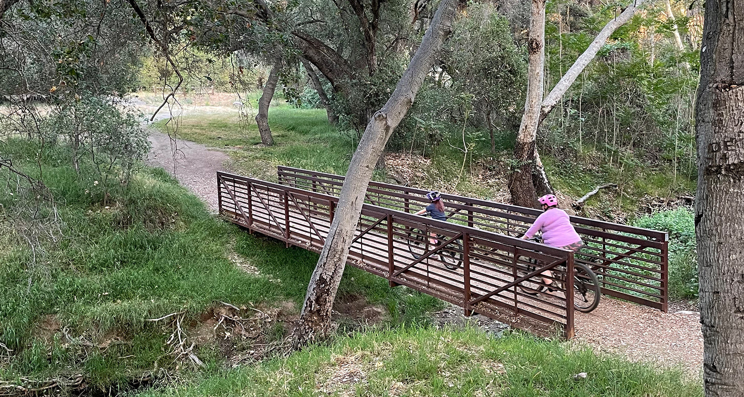 Mother and daughter mountain biking over bridge