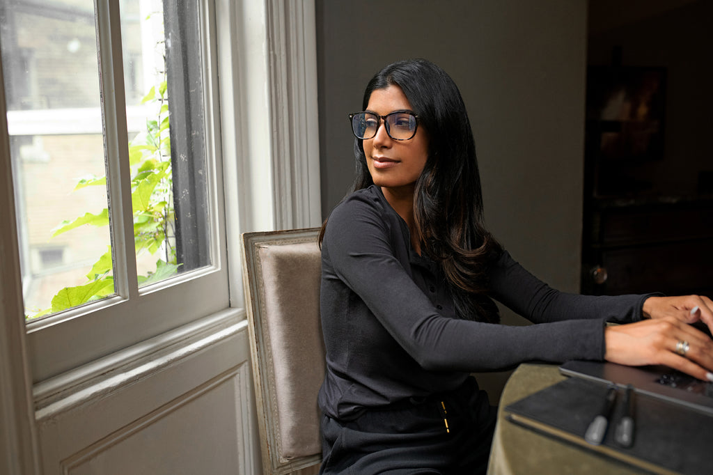 Woman wearing glasses and a black long sleeve top sitting at a table working from home
