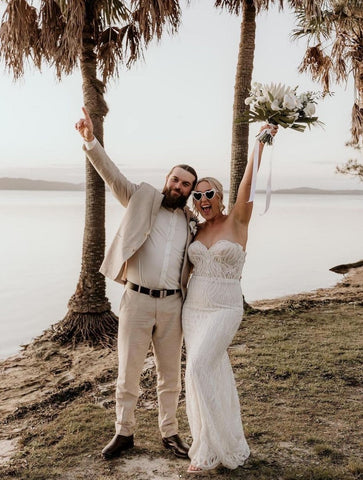 bride and groom on beach arms up holding flowers on beach